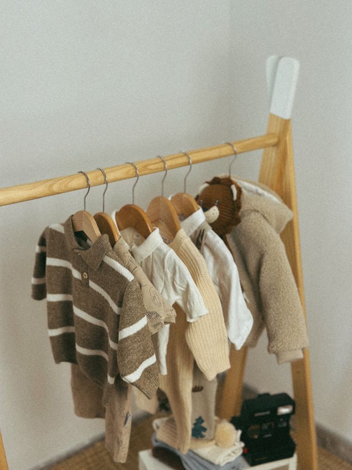 Home Warm neutral-toned baby clothes hanging on a wooden rack in a nursery.